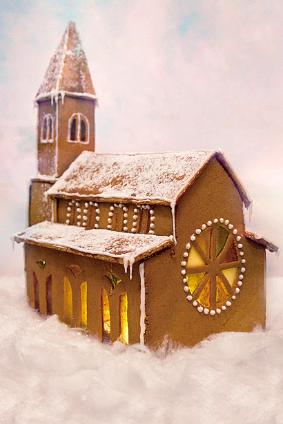Foto av pepparkakskyrkan sedd bakifrån. Den har snedtak och ett kyrktorn. Längst bak är ett runt fönster med olikafärgade "tårbitar" omgiven av  en cirkel av vita prickar