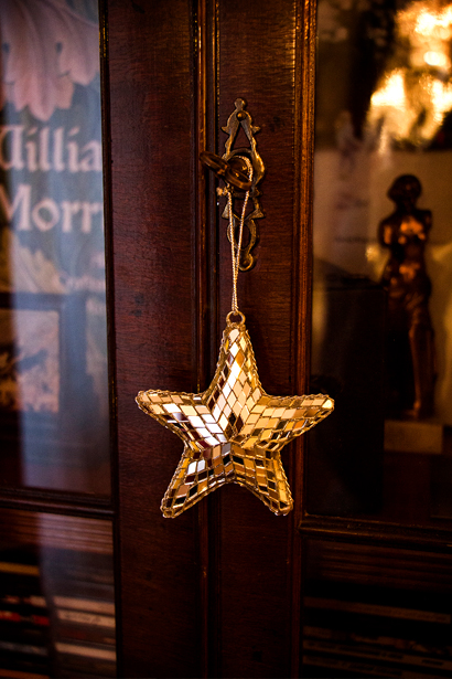 Foto av en julgransprydnad i form av en guldig stjärna som hänger på dörren till ett bokskåp. I skåpet anas en statyett av en kvinna och en bok aom William Morris