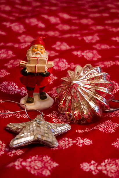 Foto av porslinstomte med julklappar som står på en röd julduk. Bredvid ligger julgranspynt.